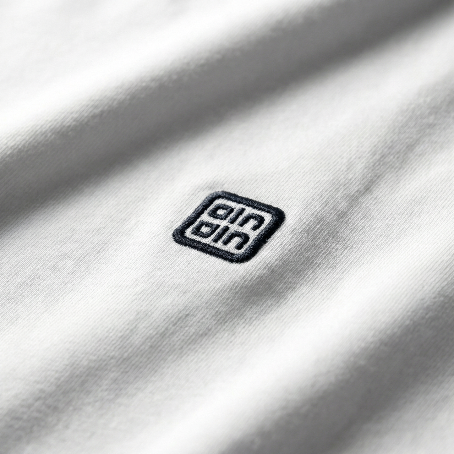 Macro detail of woven chest logo emblem on White cotton tee.