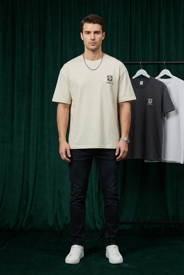 Man wearing WEARON Heritage Crest Tee in Ivory with hanging colourways behind, deep green velvet backdrop, full body.