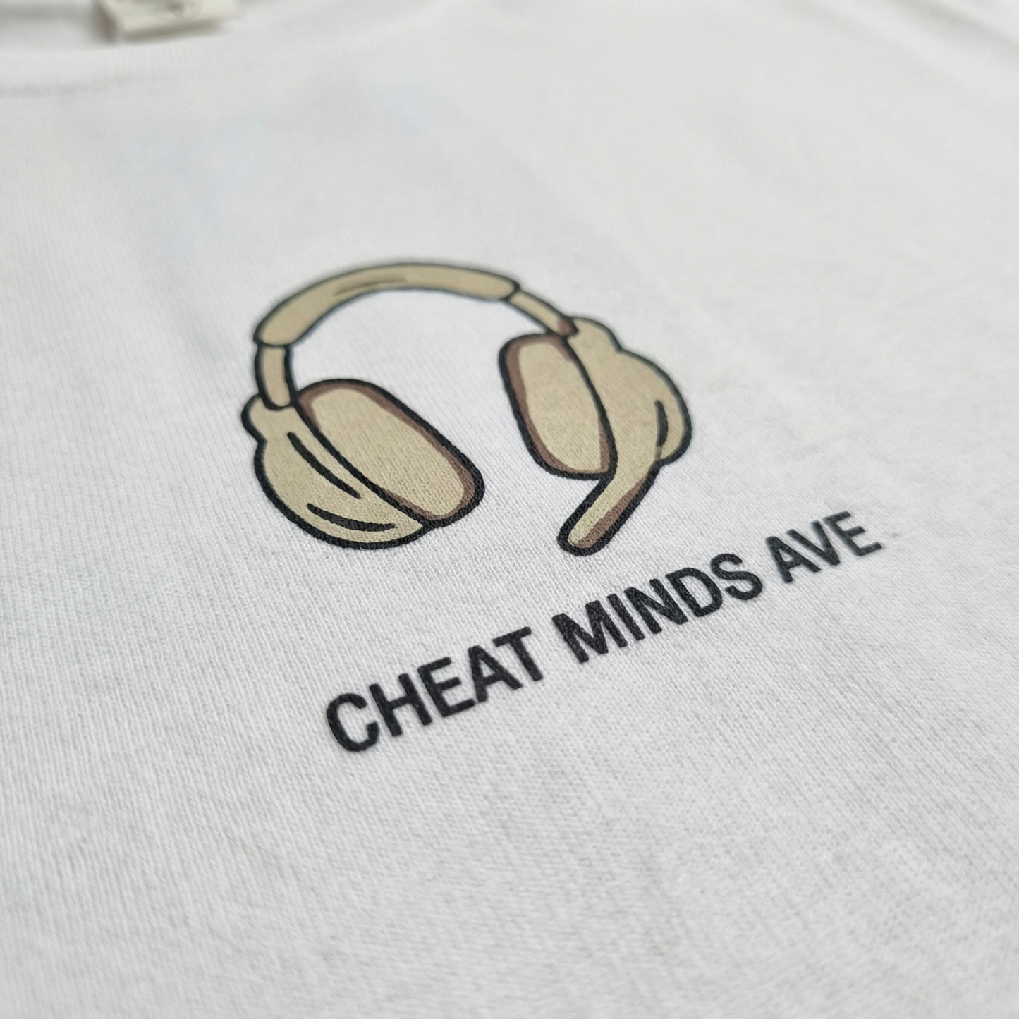 Macro detail of illustrated headphones chest motif on White cotton tee.