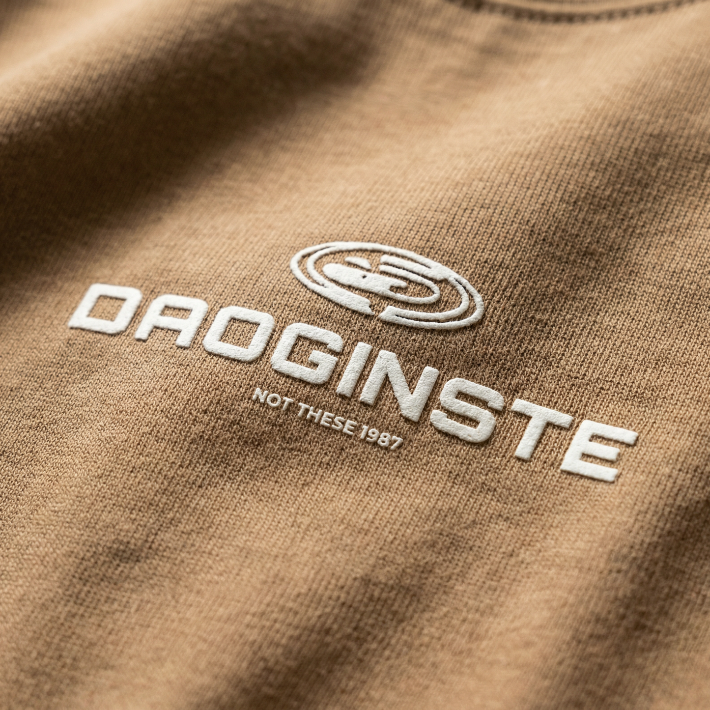 Macro detail of embroidered sport emblem on Tan cotton tee.