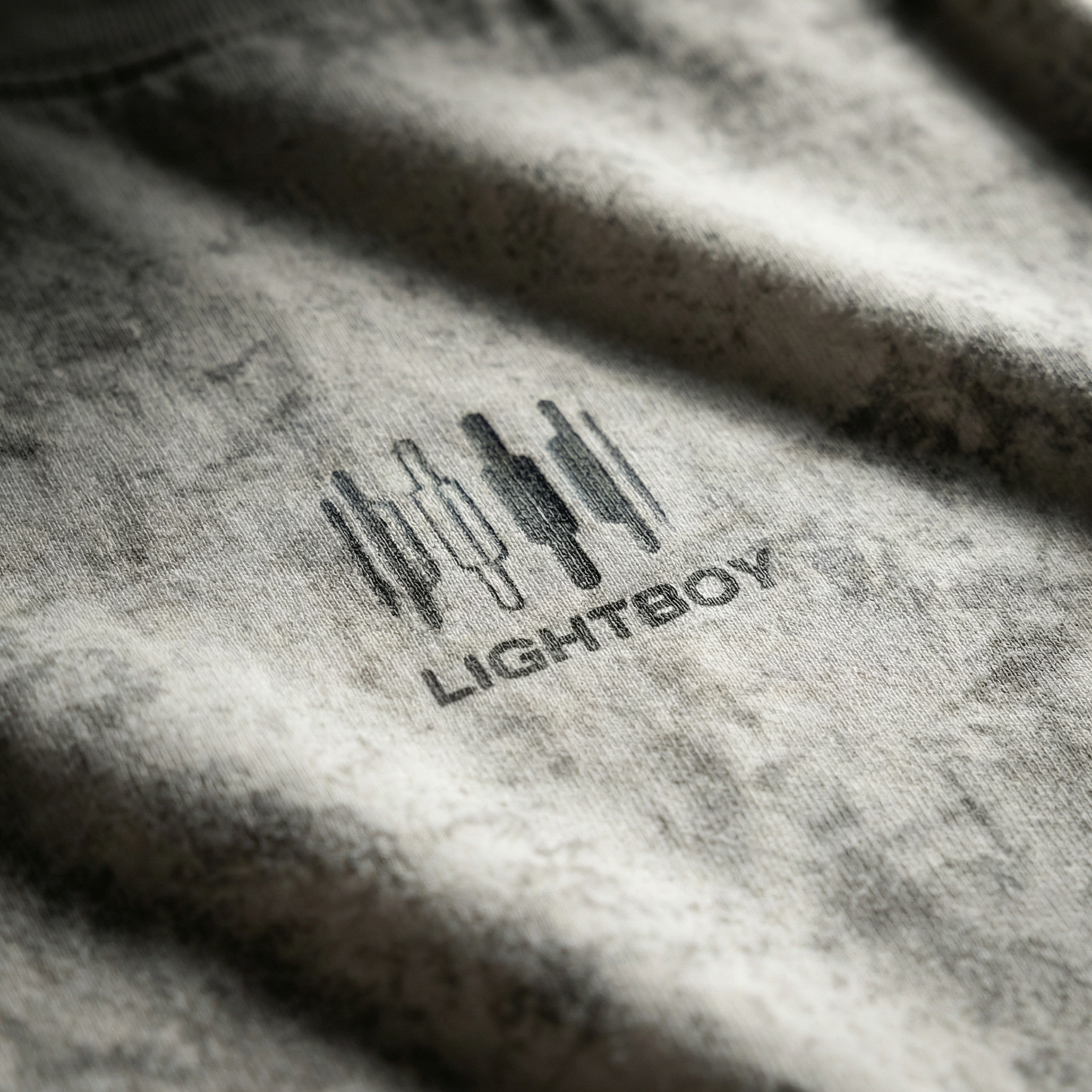 Macro detail of chest emblem and mineral-wash texture on Gray cotton tee.