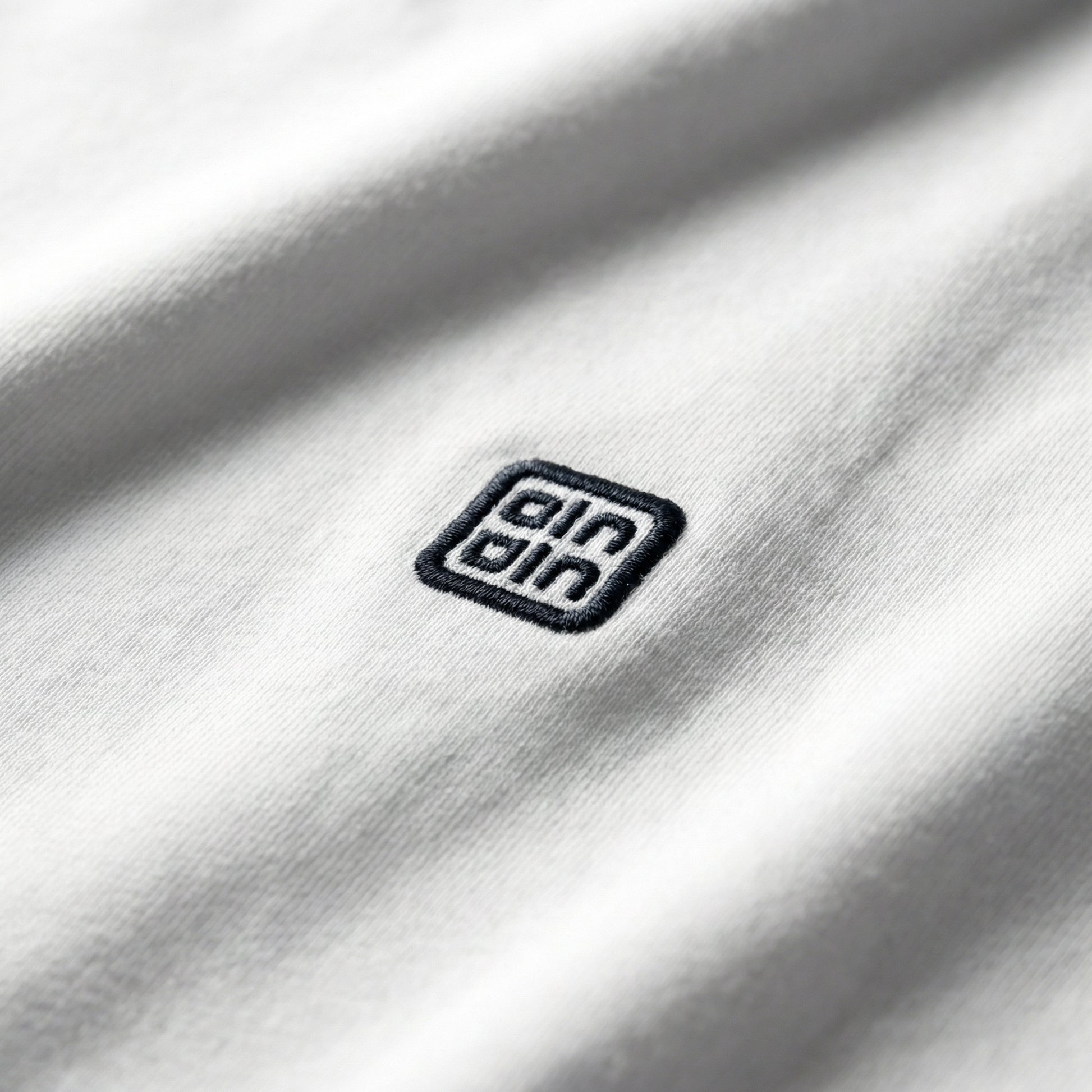 Macro detail of woven chest logo emblem on White cotton tee.