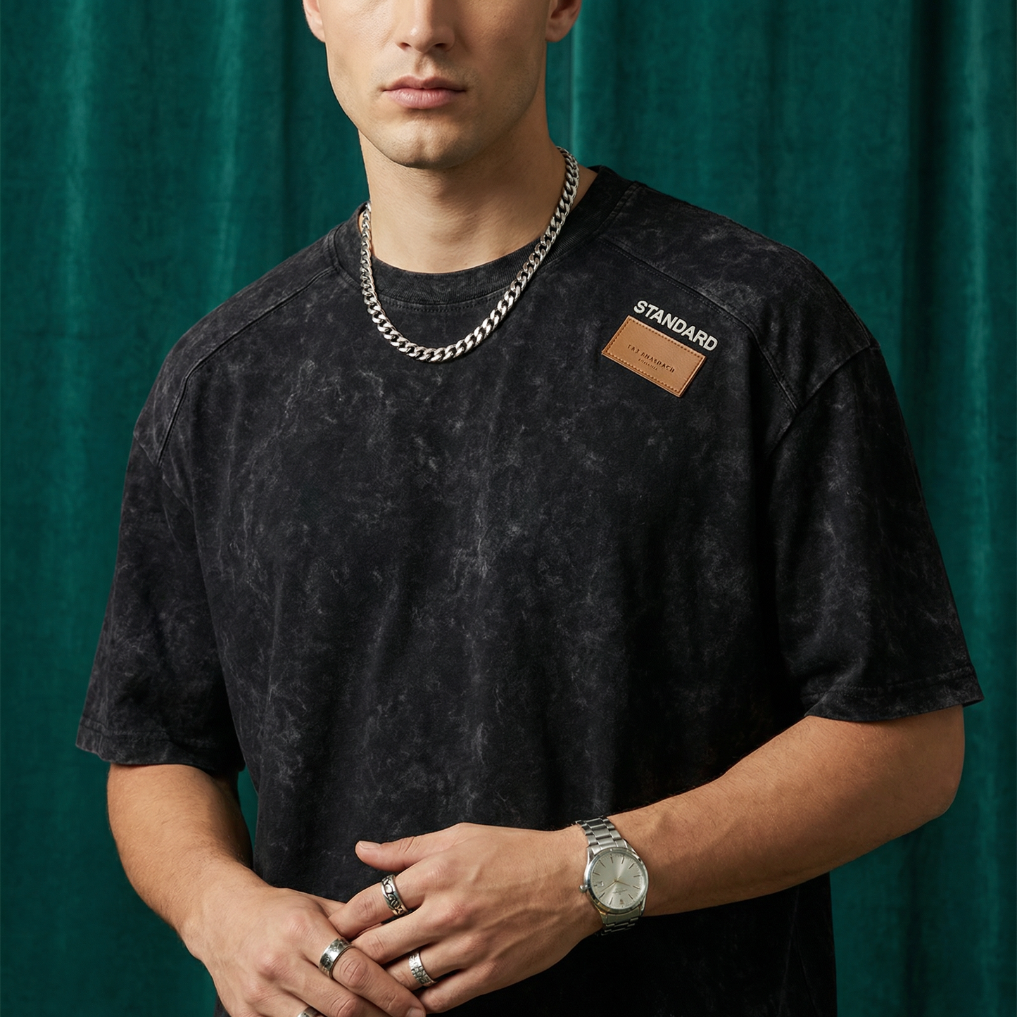 Close-up of WEARON Acid-Wash Patch Tee in Black with stitched leather shoulder patch, deep green velvet backdrop.
