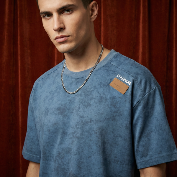 Man wearing WEARON Acid-Wash Patch Tee in Blue with rolling rack of colourways, rust velvet backdrop, full body.
