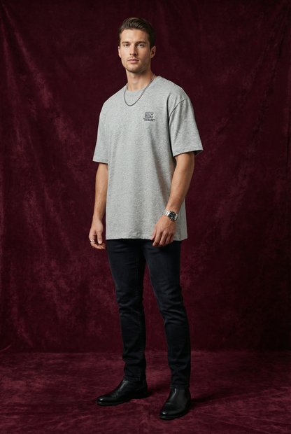 Man wearing WEARON Travelers Mountain Tee in Heather Gray, full body, deep burgundy velvet backdrop.