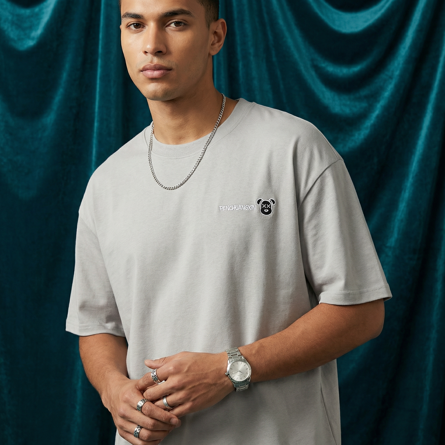 Close-up of WEARON Bear Patch Tee in Gray with embroidered bear motif, deep teal velvet backdrop.