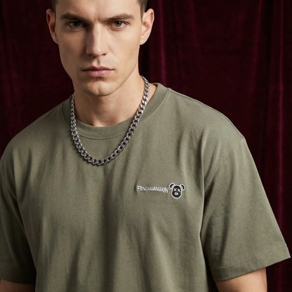Close-up of WEARON Bear Patch Tee in Olive with embroidered bear motif, deep burgundy velvet backdrop.