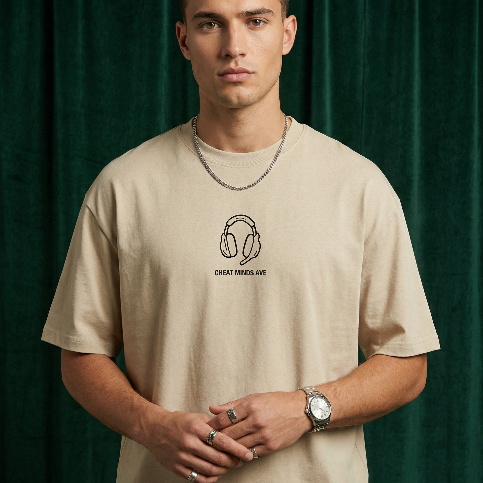 Close-up of WEARON Headphones Tee in Beige with illustrated headphones motif, deep green velvet backdrop.