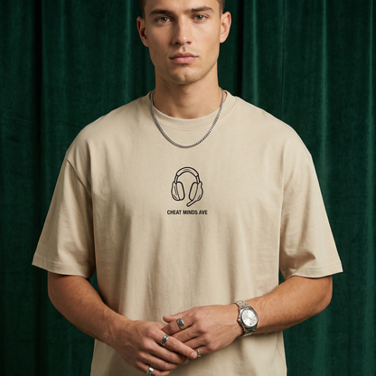 Close-up of WEARON Headphones Tee in Beige with illustrated headphones motif, deep green velvet backdrop.