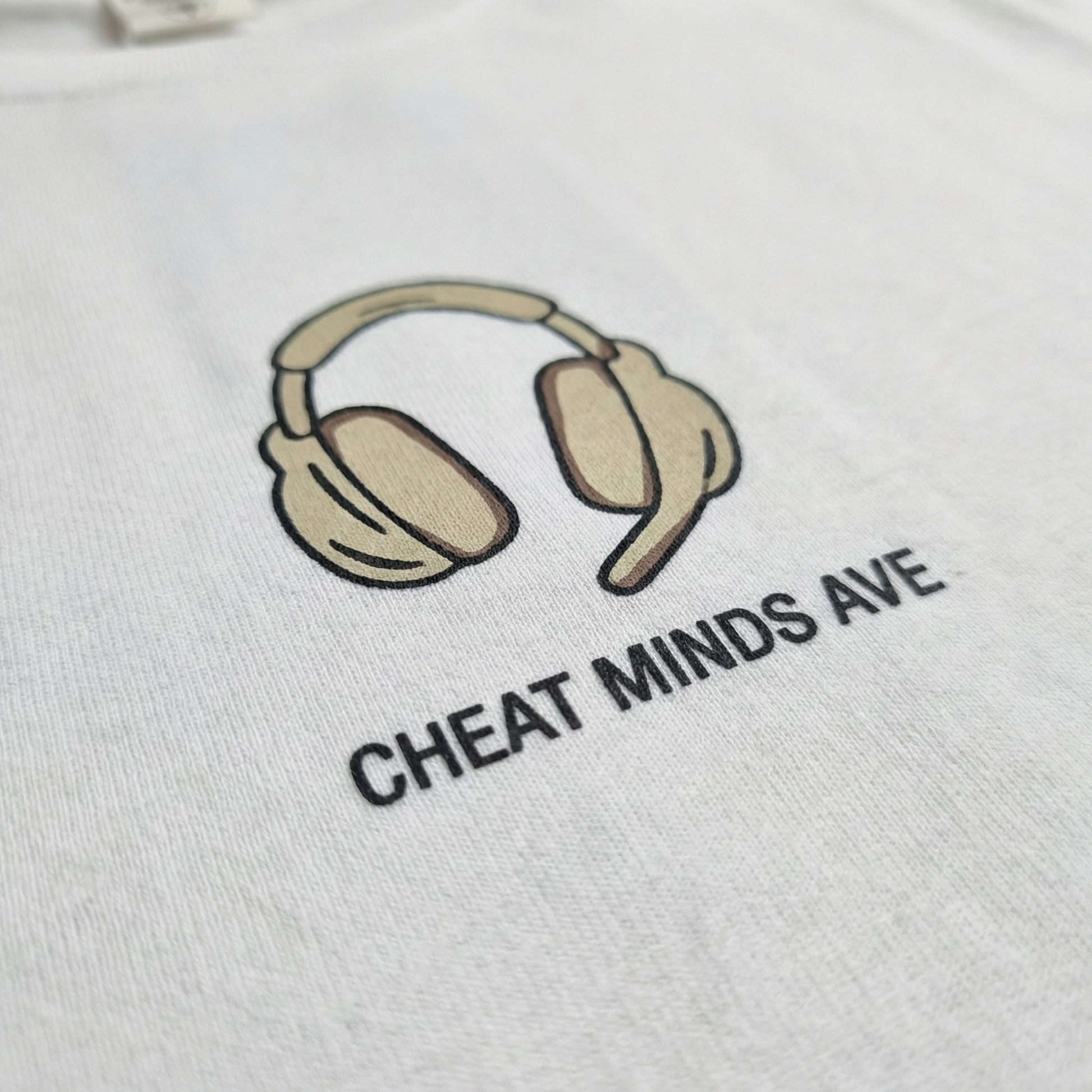 Macro detail of illustrated headphones chest motif on White cotton tee.