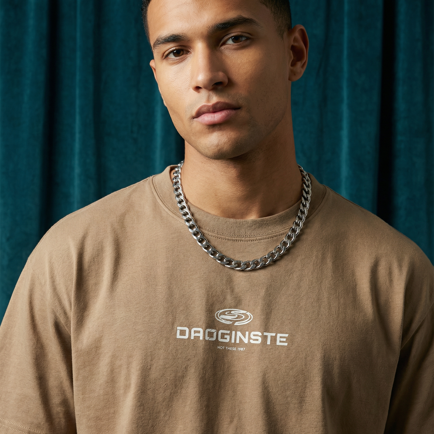 Close-up of WEARON Sport Logo Tee in Tan with chest sport emblem print, deep teal velvet backdrop.