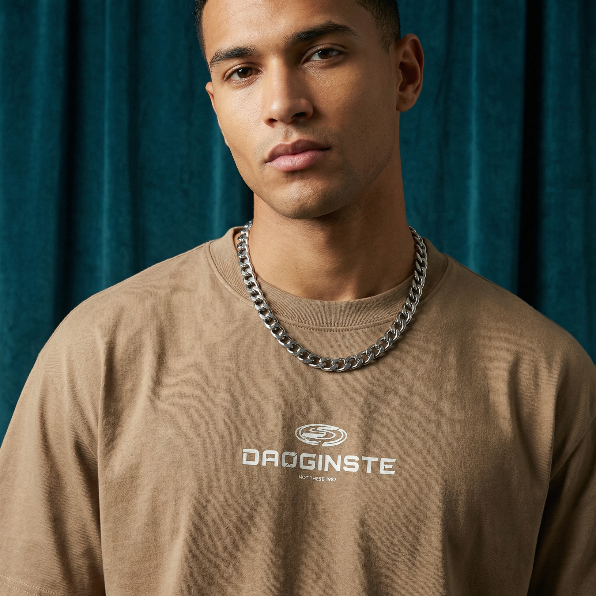 Close-up of WEARON Sport Logo Tee in Tan with chest sport emblem print, deep teal velvet backdrop.