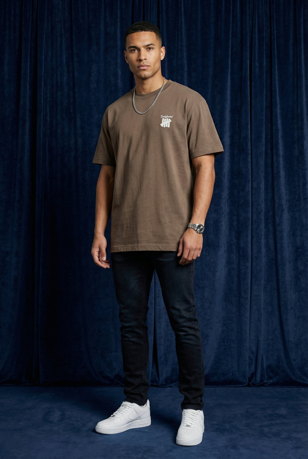 Man wearing WEARON 4-Bar Embroidered Tee in Brown, full body, deep blue velvet backdrop.