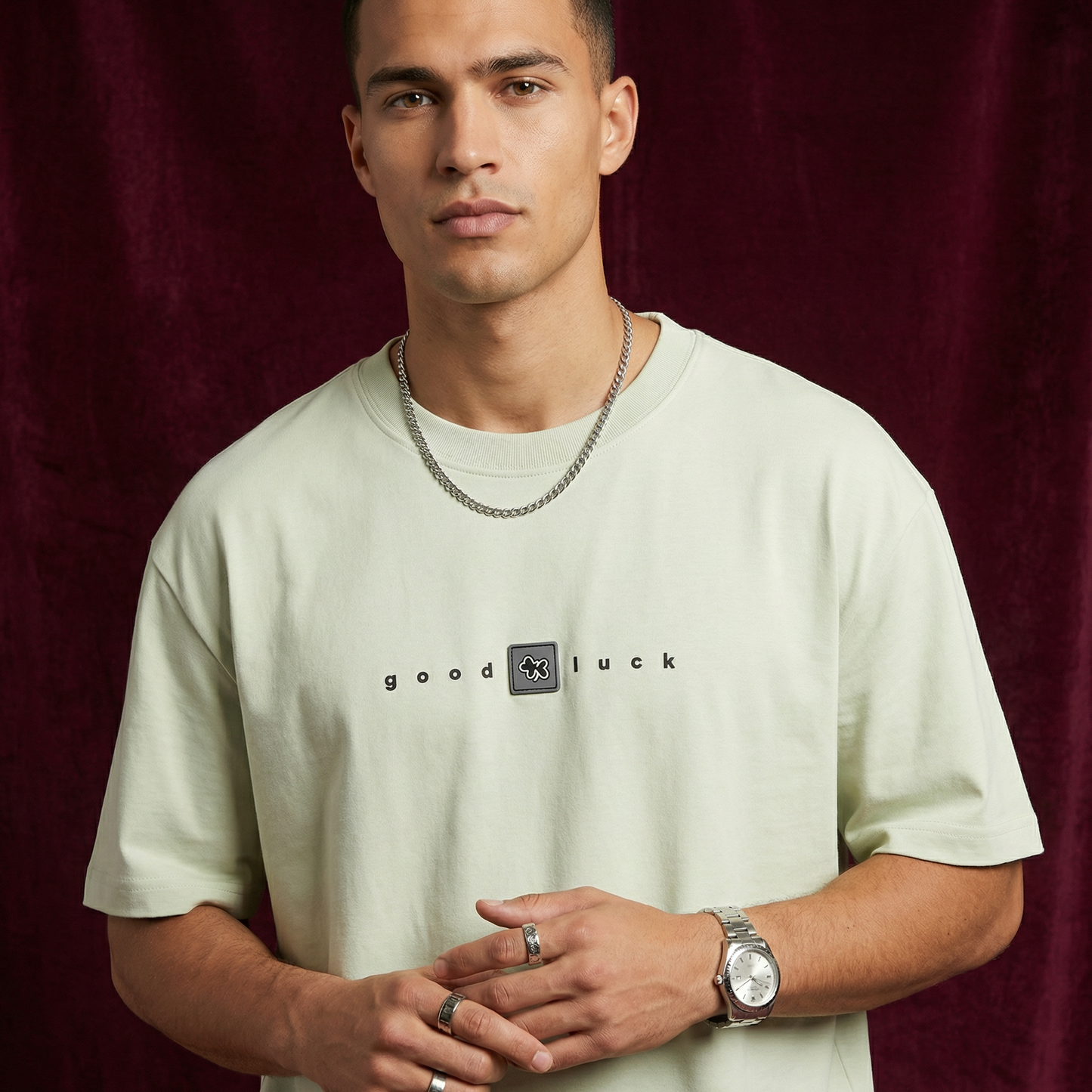 Close-up of WEARON Good Luck Tee in Sage with chest 'good luck' typography, burgundy velvet backdrop.