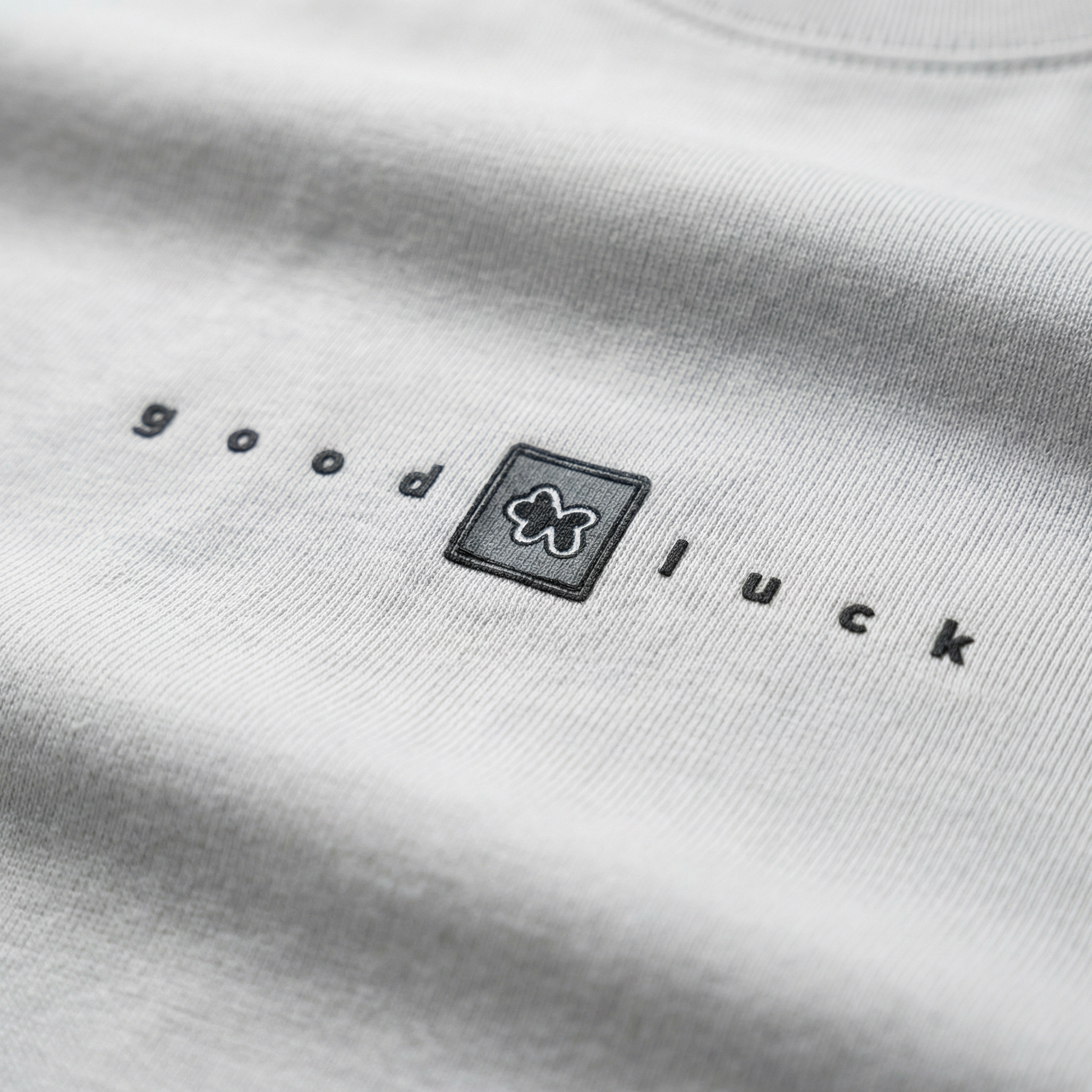 Macro detail of 'good luck' chest typography on White cotton tee.