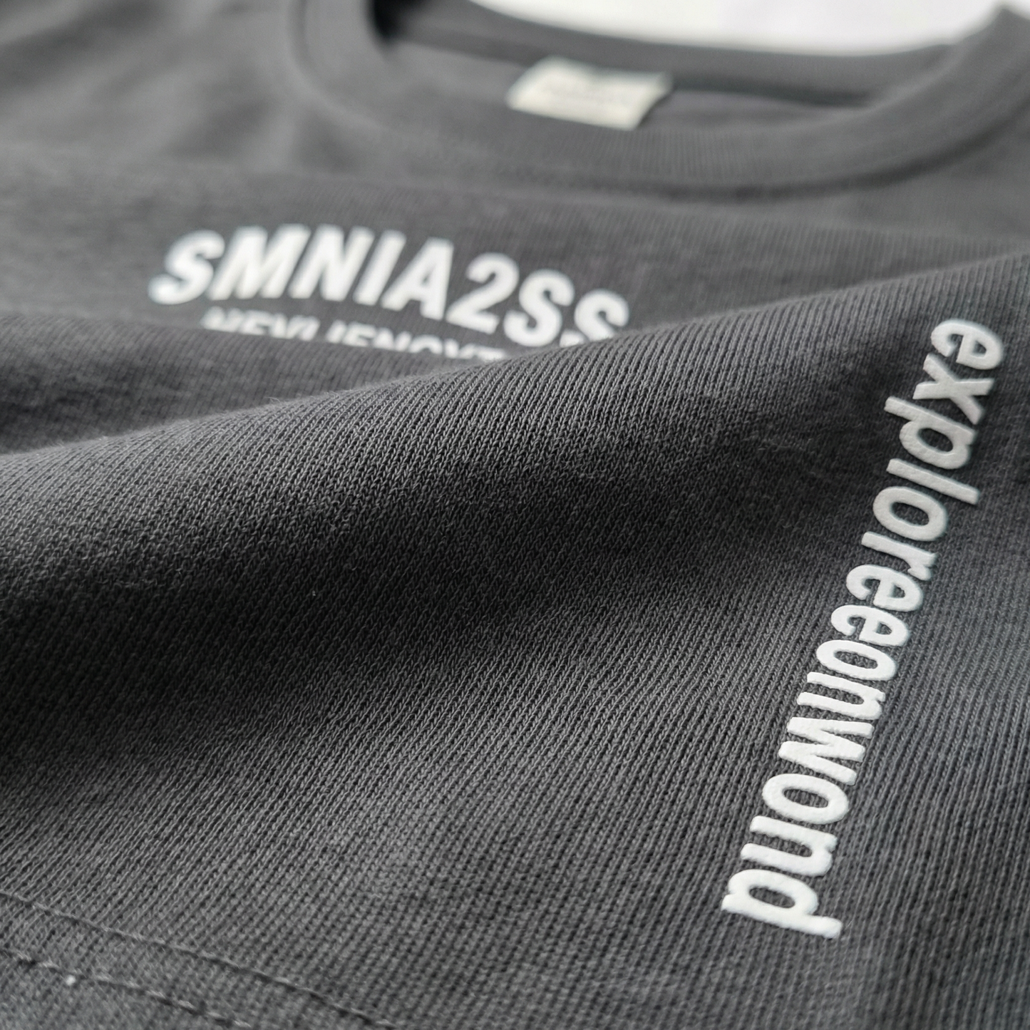 Macro detail of typographic chest print and side 'explore onward' text on Charcoal cotton tee.