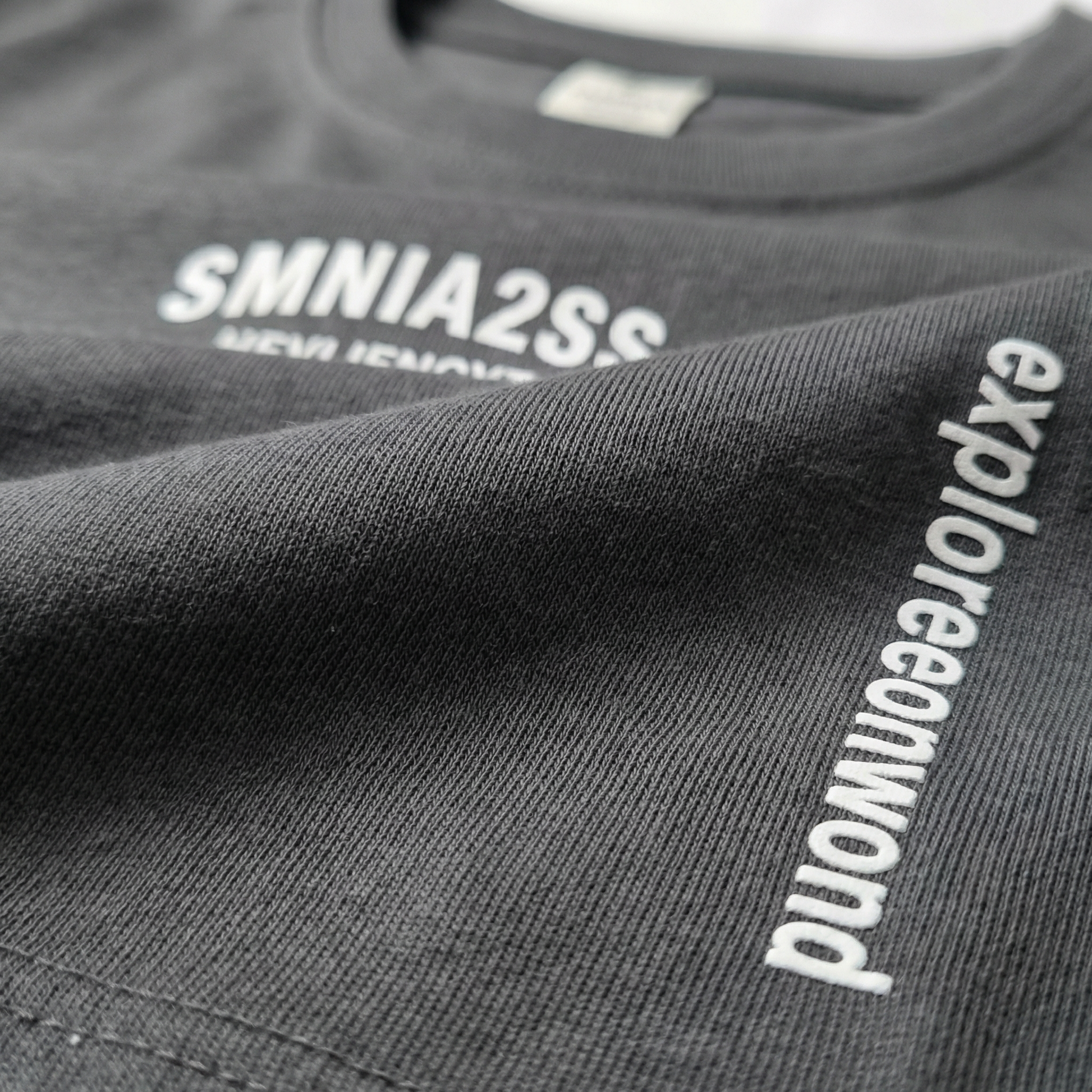 Macro detail of typographic chest print and side 'explore onward' text on Charcoal cotton tee.