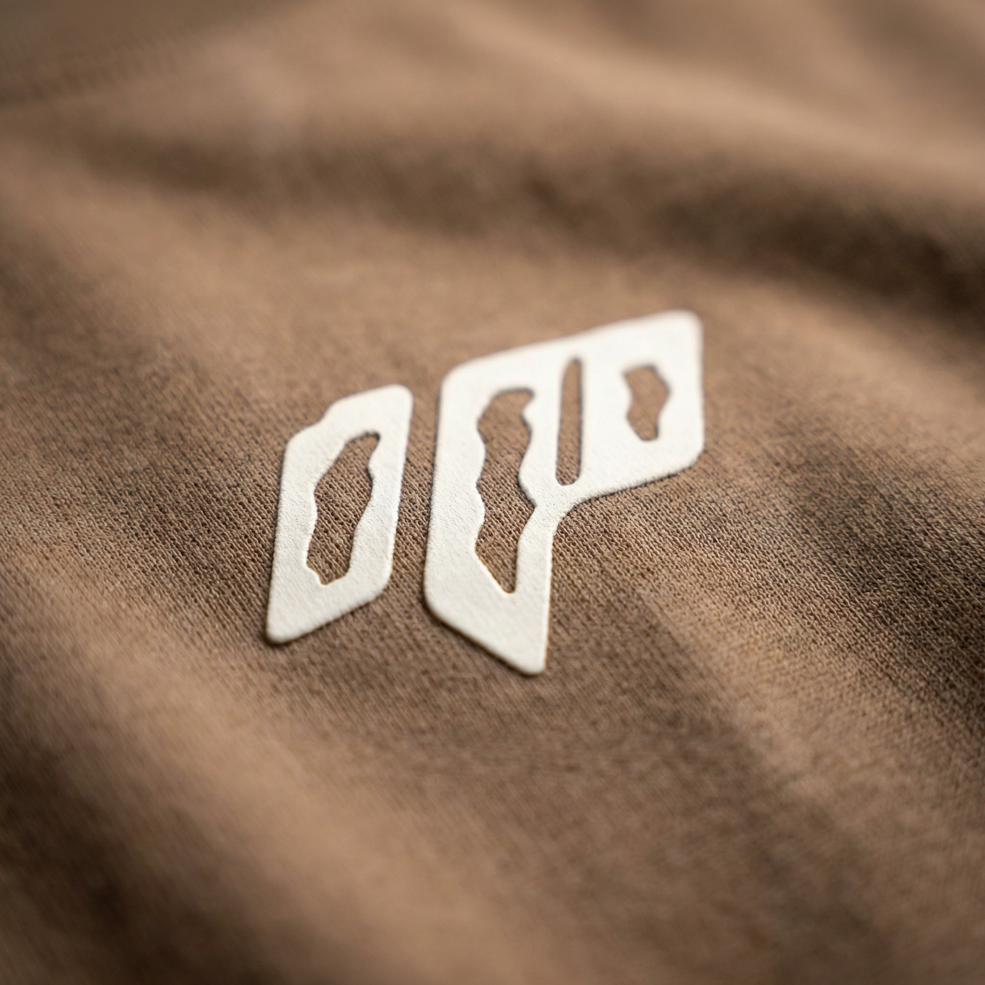 Macro detail of geometric chest emblem on Brown cotton tee.