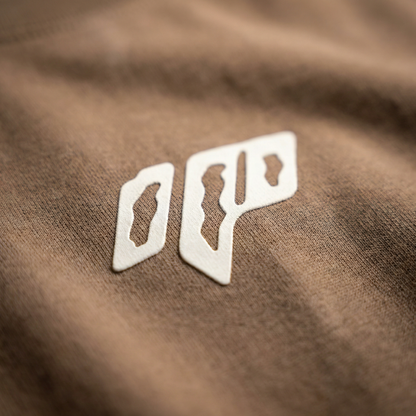 Macro detail of geometric chest emblem on Brown cotton tee.