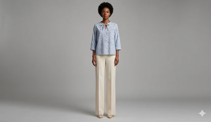 Full body view of WEARON Ribbon-Tie Dot Blouse in Light Blue with cream wide-leg trousers, soft grey studio backdrop.