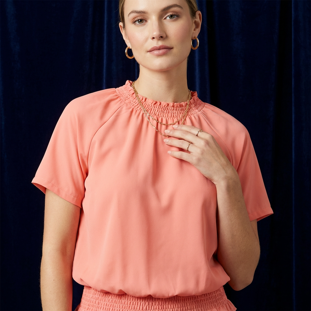 Close-up of WEARON Smocked Satin Top in Coral with smocked neckline and peplum hem, deep navy velvet backdrop.