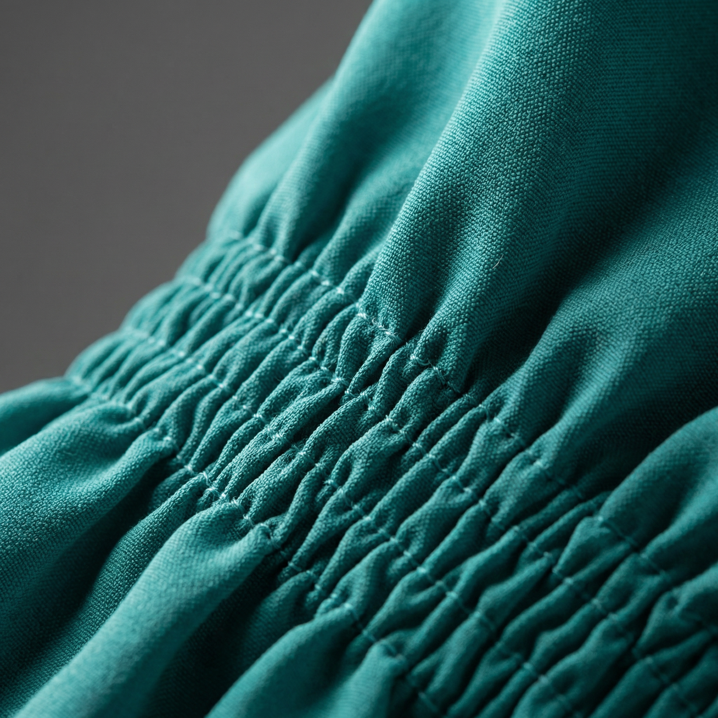 Macro detail of smocked elastic stitching on Teal silk-touch satin top.