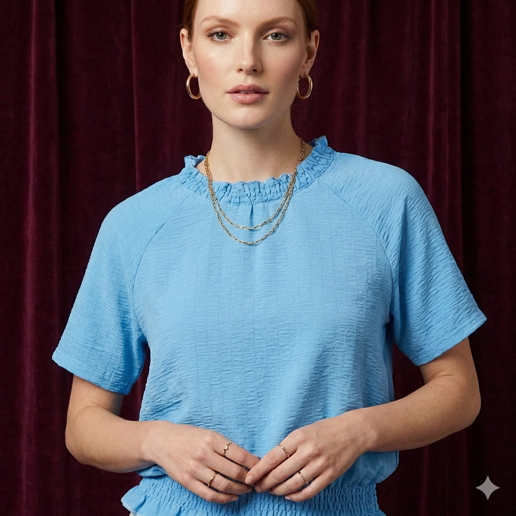 Close-up of WEARON Smocked Cotton Top in Light Blue with textured cotton fabric and smocked ruffle neckline, deep purple velvet backdrop.