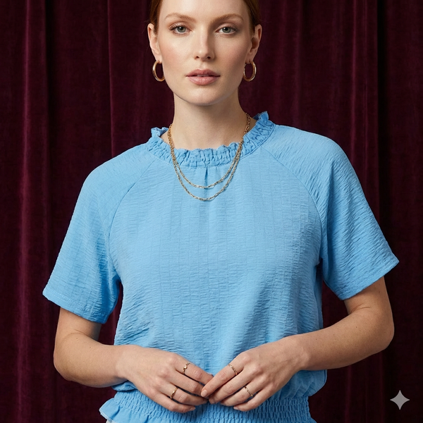Close-up of WEARON Smocked Cotton Top in Light Blue with textured cotton fabric and smocked ruffle neckline, deep purple velvet backdrop.
