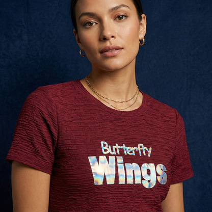 Close-up of WEARON Iridescent Slogan Mini Dress in Burgundy with iridescent Butterfly Wings graphic, navy backdrop.