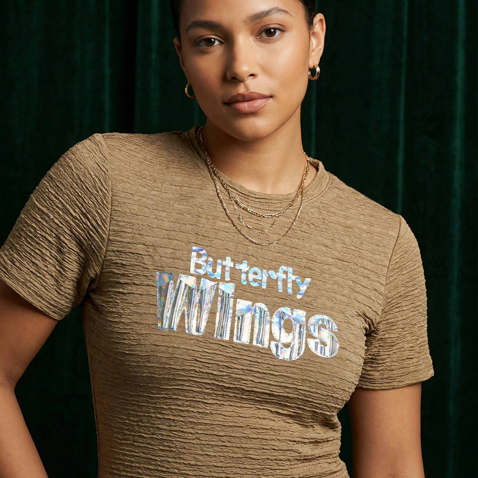 Close-up of WEARON Iridescent Slogan Mini Dress in Olive with iridescent Butterfly Wings graphic, deep green velvet backdrop.
