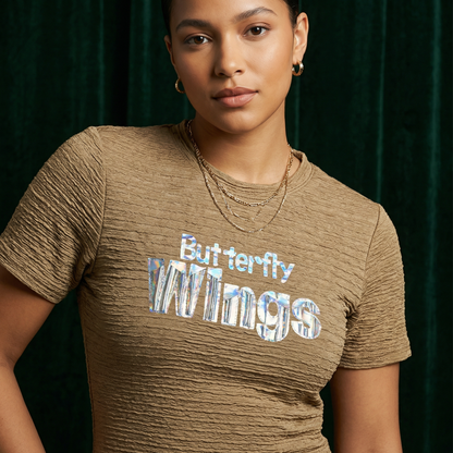 Close-up of WEARON Iridescent Slogan Mini Dress in Olive with iridescent Butterfly Wings graphic, deep green velvet backdrop.