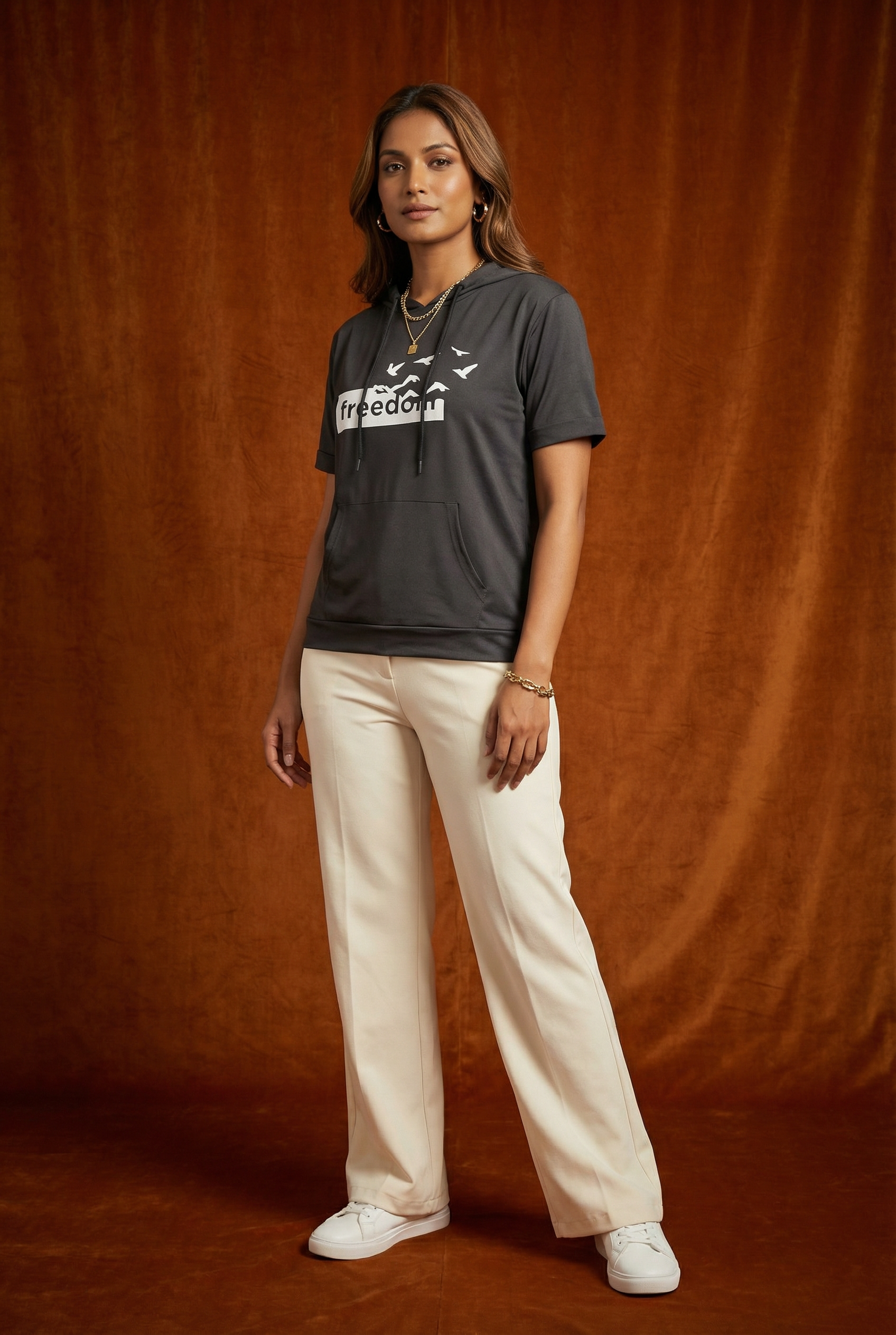 Full body view of WEARON Short-Sleeve Hoodie Tee in Charcoal with Freedom birds graphic, cream wide-leg trousers, rust velvet backdrop.