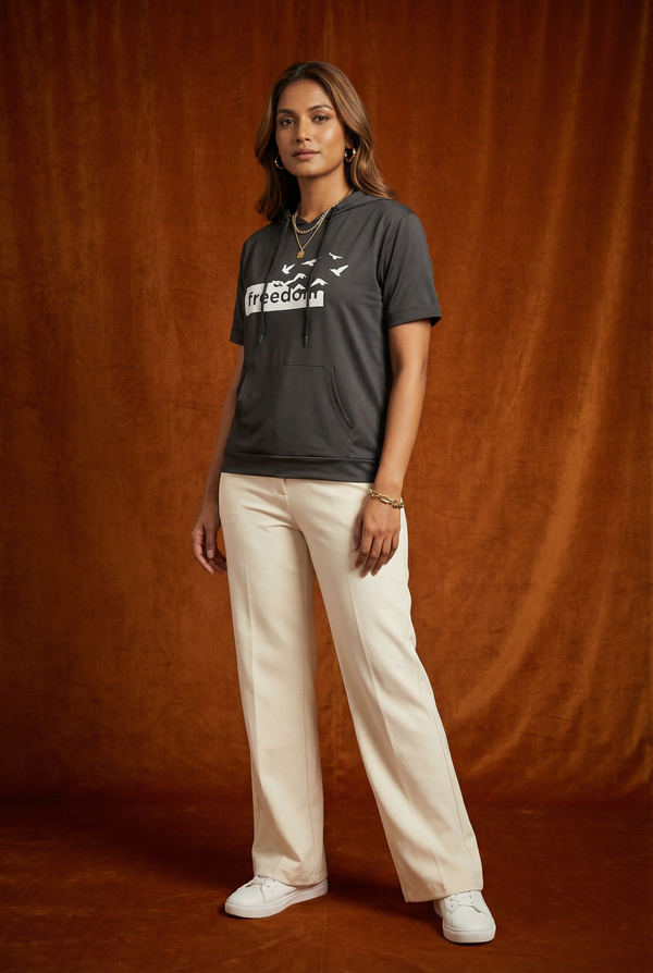 Full body view of WEARON Short-Sleeve Hoodie Tee in Charcoal with Freedom birds graphic, cream wide-leg trousers, rust velvet backdrop.