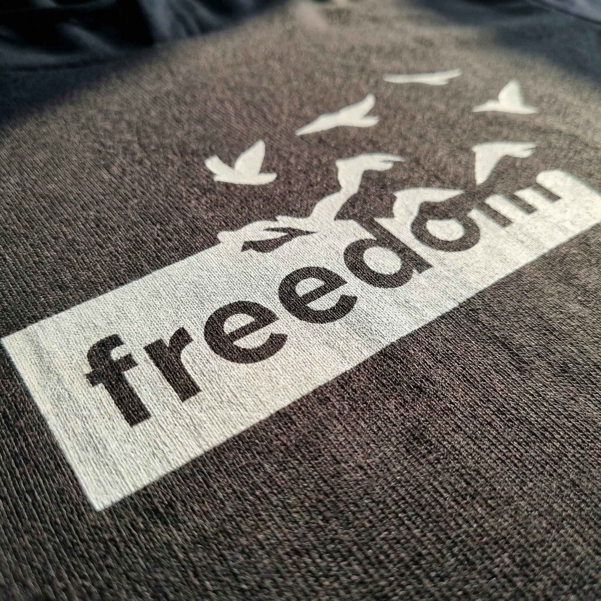 Macro detail of Freedom birds graphic on Charcoal cotton hoodie tee.