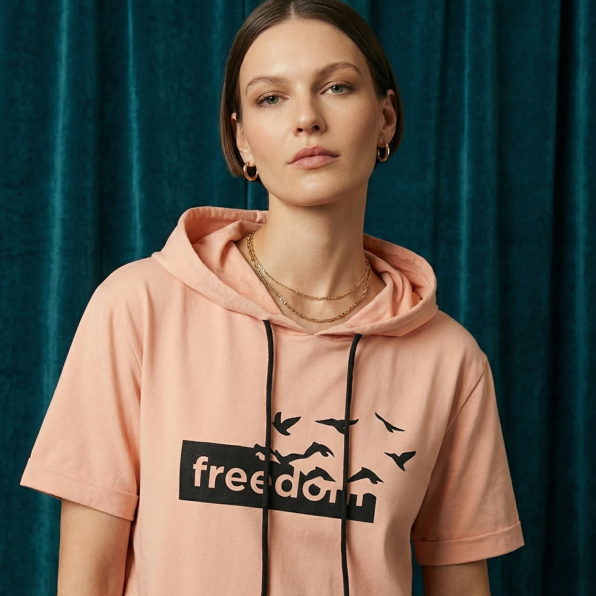 Close-up of WEARON Short-Sleeve Hoodie Tee in Peach with Freedom birds graphic, teal velvet backdrop.