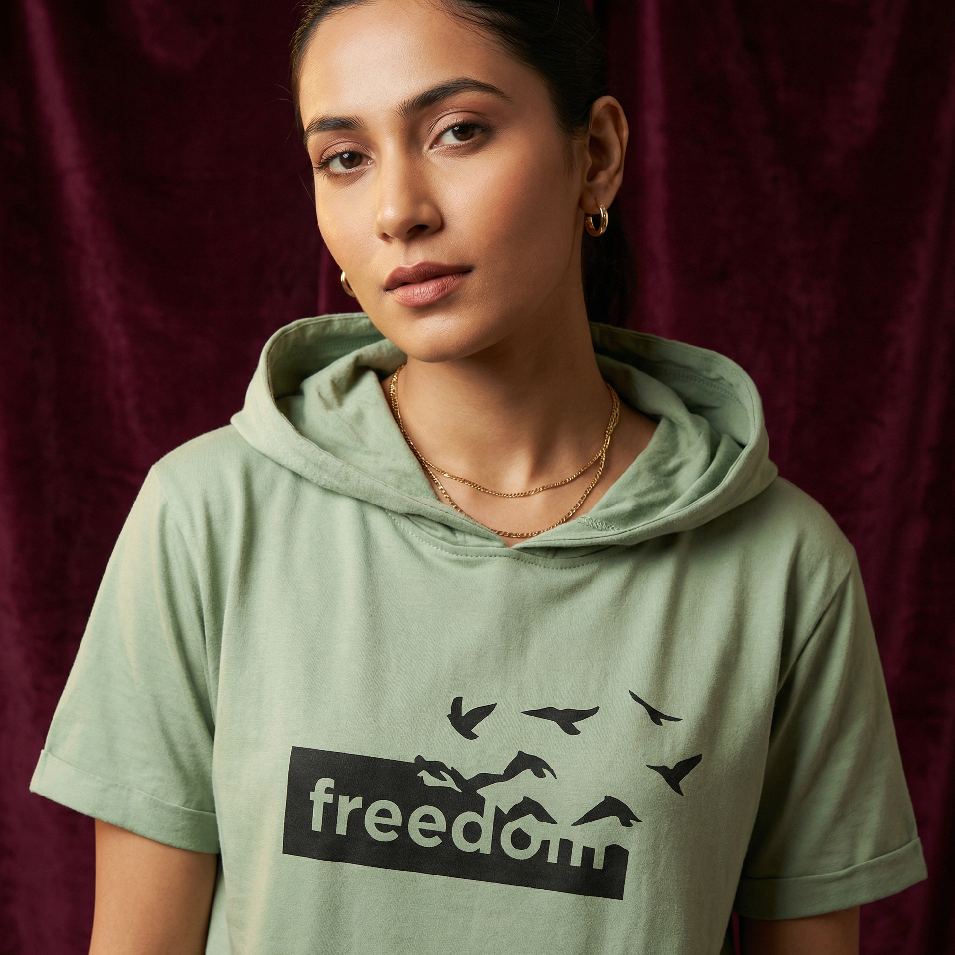Close-up of WEARON Short-Sleeve Hoodie Tee in Sage with Freedom birds graphic, burgundy velvet backdrop.