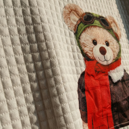 Macro detail of waffle-quilted ivory texture and Aviator teddy pilot graphic.
