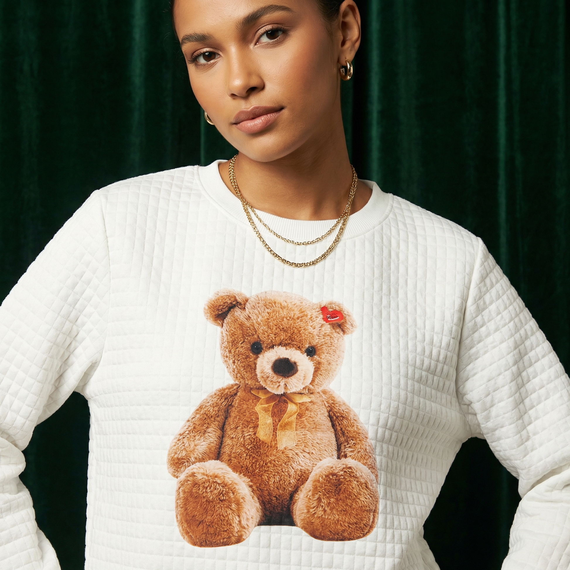 Close-up of WEARON Teddy Bear Quilted Sweatshirt with Classic teddy bear graphic, deep green velvet backdrop.