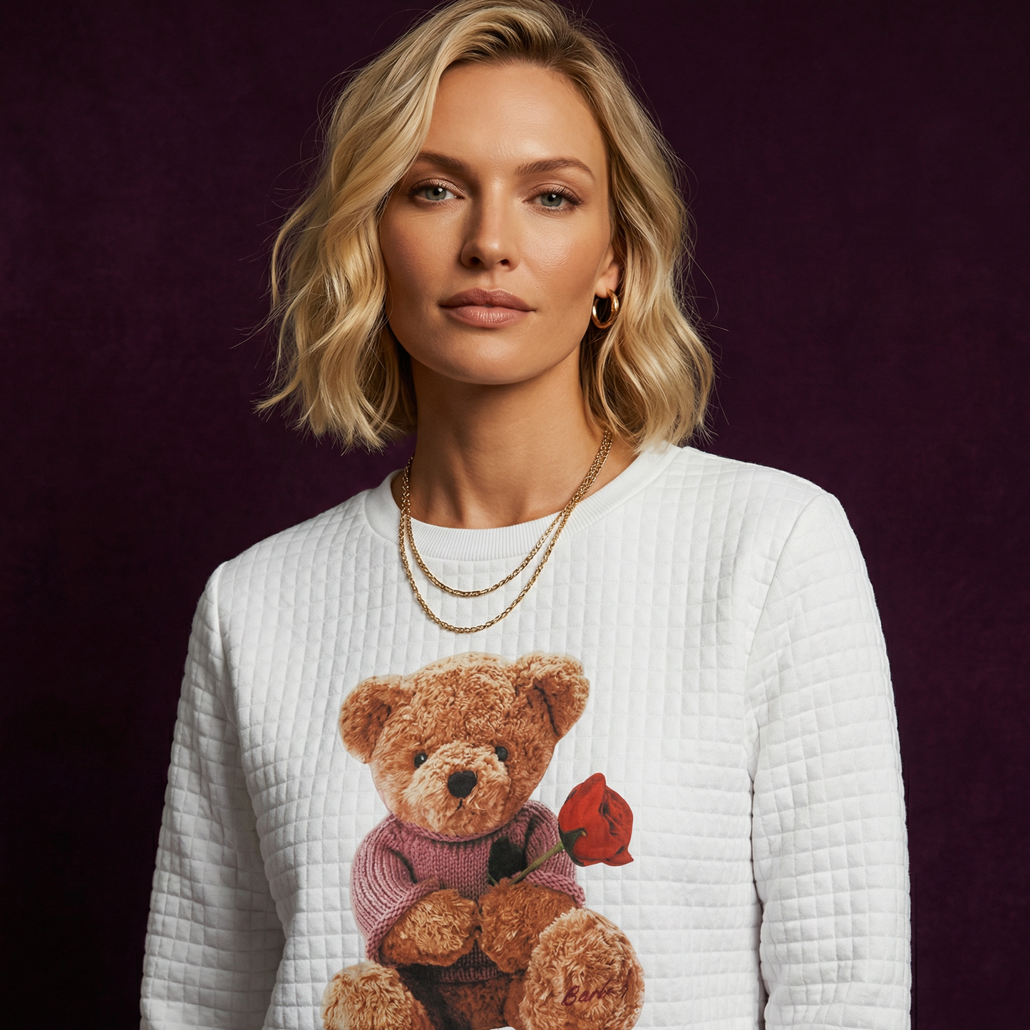 Close-up of WEARON Teddy Bear Quilted Sweatshirt with Rose-bearing teddy graphic, deep purple velvet backdrop.