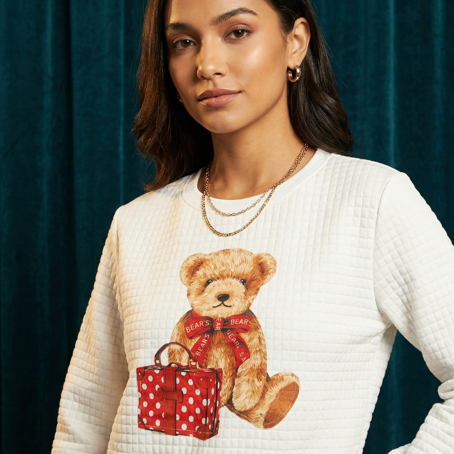 Close-up of WEARON Teddy Bear Quilted Sweatshirt with Travel teddy graphic featuring Bear-branded shopping bags, teal velvet backdrop.
