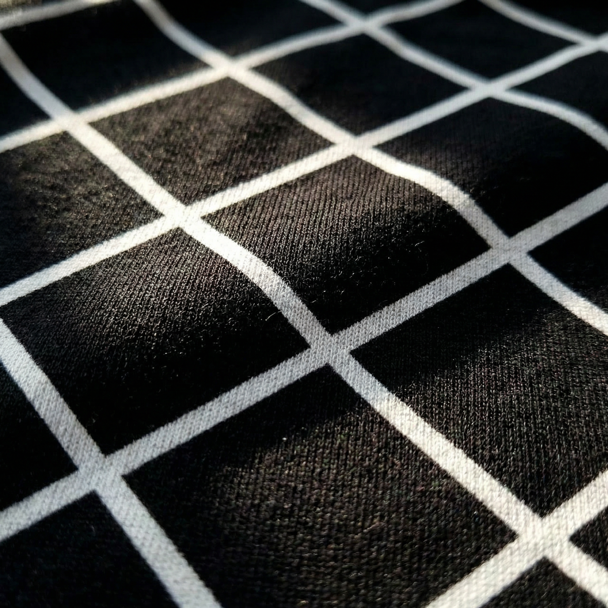 Macro detail of bias-set white windowpane lattice print on Black cotton tee, soft-touch fabric texture.