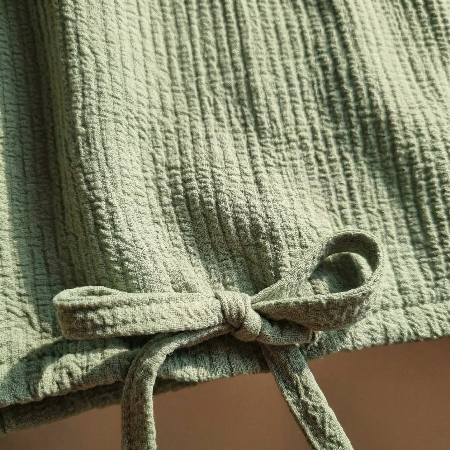 Macro detail of self-drawstring bow at hem of Sage textured cotton top.