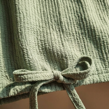 Macro detail of self-drawstring bow at hem of Sage textured cotton top.